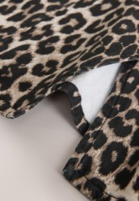 Gros plan d'un tissu plié avec un motif léopard beige et noir sur une surface lisse.