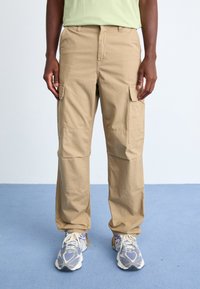 Beige Cargo-Hose mit multifunktionalen Taschen, aus leichtem Material, mit lockerer Passform und geradem Bein.