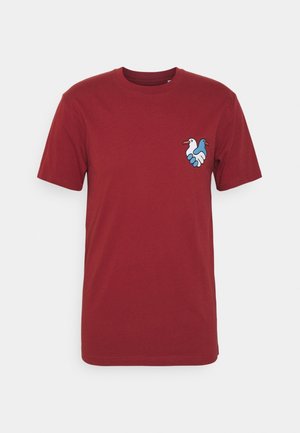 Maglietta rossa in cotone con una piccola grafica di un uccello blu e bianco sul lato sinistro del petto. Scollo rotondo e maniche corte.
