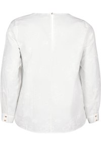 Blusa bianca a maniche lunghe con motivo floreale texturizzato, colletto rotondo, chiusura con bottoni sul retro e polsini con bottoni. Finitura in tessuto morbido.
