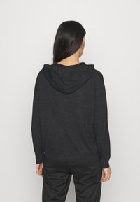 Tmavě šedá mikina s volným střihem, obsahující přední kapsu a nastavitelnou šňůrku, vyrobená z měkké texturované látky.