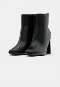 Černé kožené kotníkové boty s blokovými podpatky a bočním zipem, zobrazené zepředu na bílém pozadí.