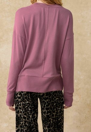 Rosa gestrickter Pullover mit einem gerippten Saum und Bündchen, der eine lockere Passform und überschnittene Schultern aufweist. Kombiniert mit schwarzen Leopardenmuster-Hosen.