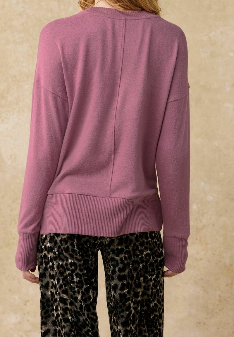 Różowy sweter dziany z prążkowanym dołem i mankietami, charakteryzujący się luźnym krojem i opuszczonymi ramionami. W zestawieniu z czarnymi spodniami w panterkę.