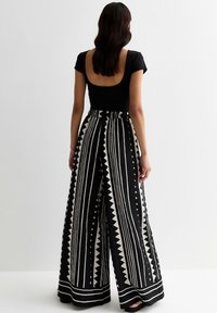 Zwart nauwsluitend topje met een lage rug, gecombineerd met brede zwart-witte broek met verticale strepen en driehoekige accenten.