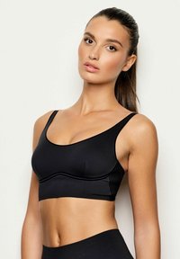Il reggiseno sportivo nero presenta un tessuto liscio, spalline larghe e un colletto rotondo. Contiene un sottile dettaglio a costine lungo i lati.