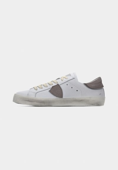 Λευκό sneaker χαμηλού πάτου με μπεζ κορδόνια, γκρι ταμπελάκι από σουέντ στη φτέρνα και γκρι επιφάνεια στο πλάι, με φθαρμένη λαστιχένια σόλα σε εκρού απόχρωση.