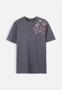 T-shirt en coton gris à manches courtes, présentant une broderie florale en rose et crème sur l'épaule gauche. Col rond.