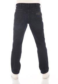 Pantalones de mezclilla azul oscuro con corte recto, cinco bolsillos y un parche de cuero en la cintura trasera. Usados con zapatillas blancas.
