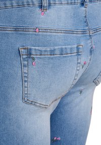 Gaiši zili džinsi ar rozā ziedu izšuvumiem aizmugures kabatās, piedāvājot klasisku piecu kabatu dizainu un smalkus izšuvumu elementus.