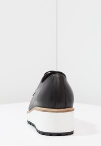 Black leather shoe with a rounded heel, featuring a white platform and textured rubber sole. Smooth finish with subtle stitching detail.