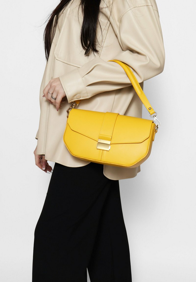 Borsa gialla con design strutturato, in morbido materiale in pelle sintetica e chiusura a pattina anteriore. Presenta una tracolla staccabile e finiture in oro.