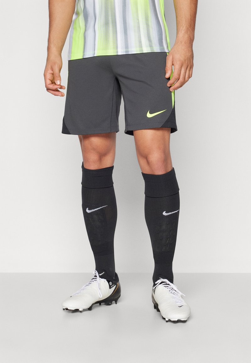 Nike Sportshorts in Dunkelgrau, kombiniert mit schwarzen knielangen Socken mit dem Logo und weißen Fußballschuhen mit schwarzen Akzenten.