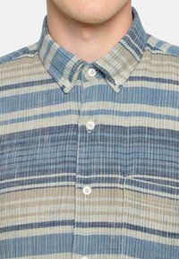 Camisa de botones a rayas con diferentes tonos de azul y beige, con un tejido texturizado y un diseño de cuello clásico.