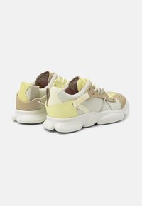 Sneakers with a yellow, beige, and cream color scheme. Features a mix of materials, rounded sole, and detailed stitching.