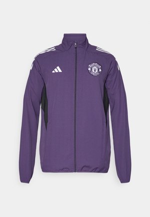 Jachetă violet cu fermoar, confecționată dintr-un material ușor, având panouri laterale negre, dungi albe adidas și un logo Manchester United pe piept.