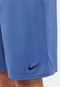 Μπλε αθλητικό σορτς με μαύρο λογότυπο Nike κεντημένο κοντά στο τελείωμα, που φοριέται στο πόδι ενός ατόμου με εμφανές δέρμα και τρίχες.