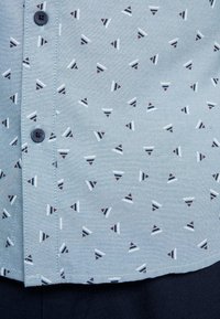 Button-up shirt van lichtblauwe stof met een klein, multikleurig driehoekpatroon. Voorzien van een volledige knoopsluiting en contrasterende donkere knopen.