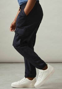 Pantalons cargo navy en tissu léger, avec des poches latérales et des poignets élastiques, associés à des baskets blanches.