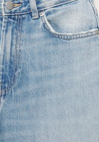 Blugi din denim albastru deschis, prim-plan, arătând buzunarul frontal cu margine uzată, buclă pentru curea și detaliu cu nasture metalic.