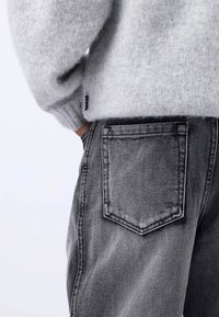 Gray knit sweater with ribbed cuffs, paired with faded black denim jeans featuring a back pocket and contrasting stitching detail.