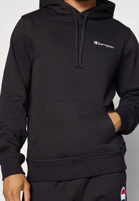 Sweat à capuche noir en tissu mélangé coton, avec une poche avant, une capuche à cordon et un petit logo brodé sur la poitrine.