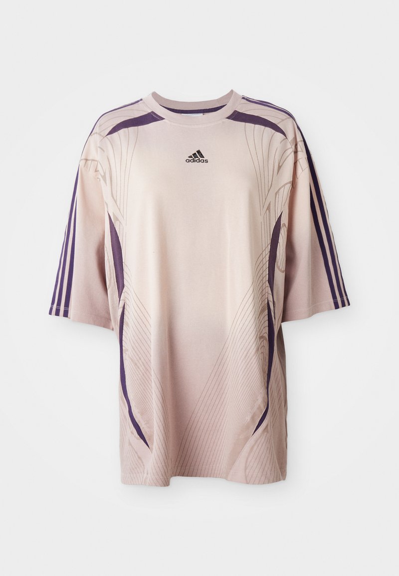 Jasnoróżowa, oversize'owa koszulka z fioletowymi akcentami i liniami wzorniczymi. Posiada krótki rękaw oraz logo Adidas na górnej części klatki piersiowej.