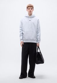 Ανοιχτό μπλε φούτερ με κουκούλα, μπροστινή τσέπη και μαύρο λογότυπο, σε συνδυασμό με μαύρο παντελόνι φαρδιάς γραμμής και μαύρη τσάντα. Λείο ύφασμα.