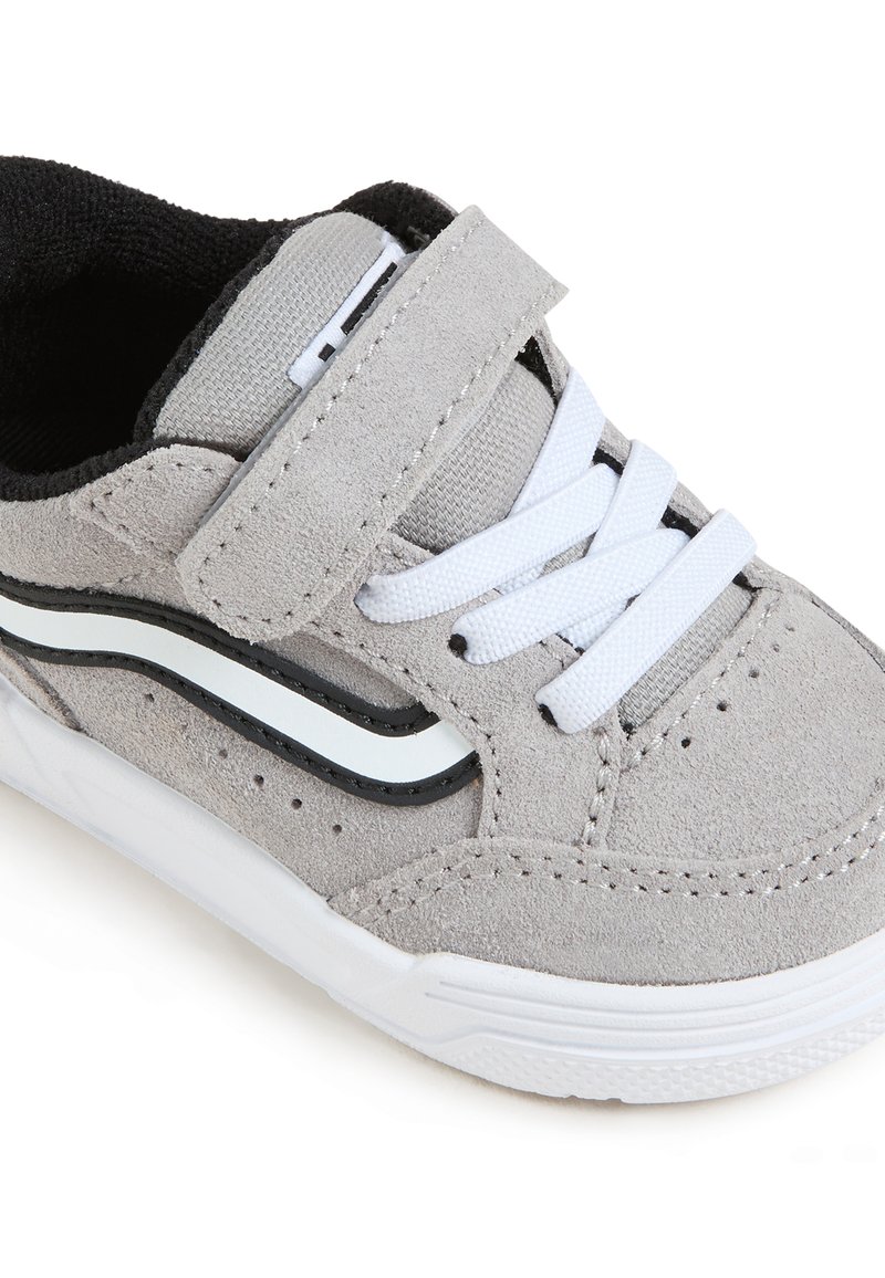 Sneaker grigio in suede con accenti neri e bianchi, dotata di una fascia in velcro, lacci bianchi e suola in gomma texturizzata con perforazioni.