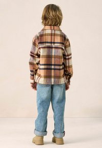 Bruin en crème geruit flanellen overhemd met een kraag, gedragen met opgerolde blauwe jeans en beige laarzen, gezien van achteren.