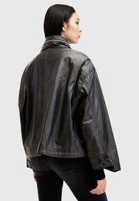 Black leather jacket with a wide collar, oversized fit, and smooth texture. Features zip closure and side pockets, paired with dark jeans.