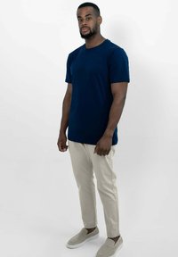 Marineblauwe t-shirt met korte mouwen, beige slim-fit broek en lichtgrijze instapschoenen. Eenvoudig ontwerp met een ronde halslijn en effen kleuren.