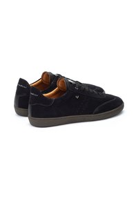 Las zapatillas de ante negro presentan un diseño de perfil bajo, un upper texturizado, acentos de cuero marrón y una suela de goma. Perforaciones sutiles en el lateral.