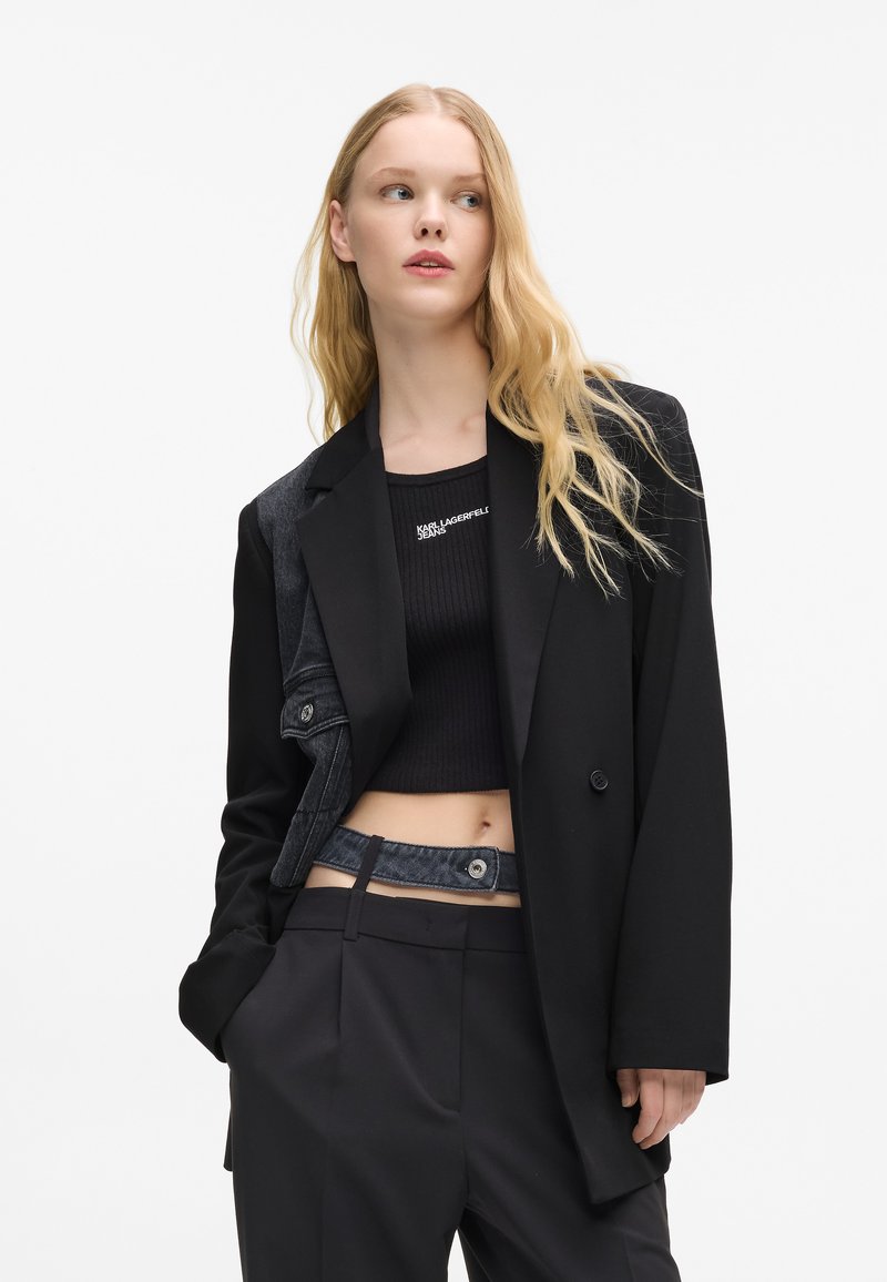 Melna žakete ar denima akcentiem, kurai ir piegriezta piegriezuma un izgriezti klāji. zem tās ir melna ribota krūšturi. Bikses ar denima jostu.