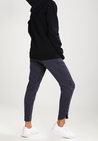 Pantalon bleu marine rayé à coupe slim, associé à un sweat à capuche noir et des baskets blanches, doté d'une taille élastique et d'ouvertures aux chevilles.
