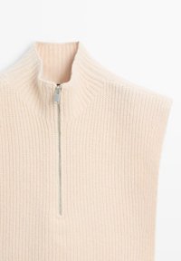 Sleeveless, high-neck knit top in light beige with ribbed texture, featuring a silver zipper closure at the front.