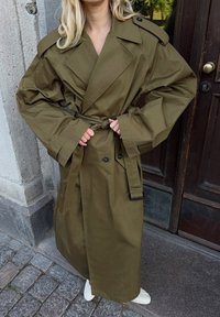 Olivza krāsas tranšejas mētelis ar jostas vidukli, lieliem lakatiem un pārmērīgiem piedurknēm, izgatavots no gludas auduma. Iekļauj divus priekšējos pogas.