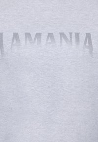 Hall hallipluus, mille rinnal on tuhmilt kontrastse kirjatüübiga sõna "ROMANIA". Valmistatud pehmest, tekstureeritud puuvillamaterjalist.