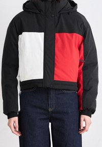 Krátká bunda s kapucí v barevném provedení černá, červená a bílá, s elastickými manžetami a kapsou na zip.