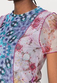 Top corto de manga corta y transparente con un patrón floral en azul y rosa, con detalles gráficos. Confeccionado en malla ligera, con ribetes en contraste.