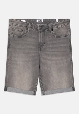 Kurzärmliges gestreiftes Hemd in Hellblau und Weiß, kombiniert mit hochgekrempelten Jeans-Shorts und weißen Turnschuhen, dazu schwarz-weiß gestreifte Socken.