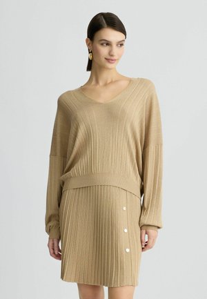 Set di maglione e gonna a righe in maglia beige. Il maglione presenta un scollo a V e maniche a caduta. La gonna ha dettagli con bottoni sui lati.