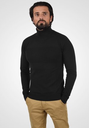 Svart polo-tröja i ribbad stickad kvalitet, åtsittande passform, med långa ärmar, kombinerad med khakifärgade byxor.