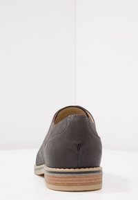 Scarpa da uomo in pelle grigia scura con superficie testurizzata, punta tonda e suola stratificata marrone chiaro. Presenta cuciture discrete lungo le cuciture.