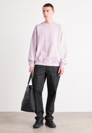 Light purple sweatshirt with embroidered "HUGO" logo, paired with dark denim pants. Model holds a black leather tote bag. Black sneakers worn.
