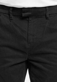 Pantalon noir avec une ceinture plate à l'avant, des passants de ceinture et une fermeture éclair avant dissimulée.