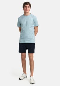 Ljusblå bomullströja med korta ärmar och rund halsringning, prydd med en liten vit logo på bröstet; matchad med marinblå shorts och sneakers.