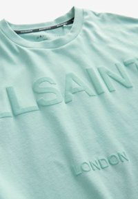 Gaiši zaļš kokvilnas T-krekls ar reljefu "ALLSAINTS" un "LONDON" tekstu, apaļu kaklu, mīkstu tekstūru un minimālisma stilu.