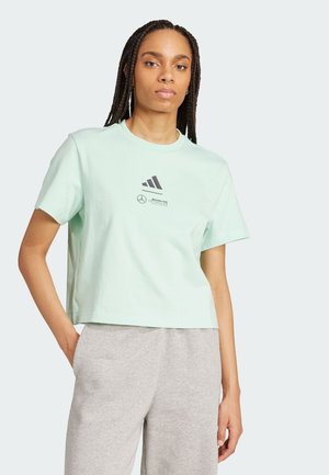Mint zelena kratka majica od mekog pamuka. Ima okrugli izrez i printani adidas logo s akcentima ispod. Uparena sa sivoj trenerkama.