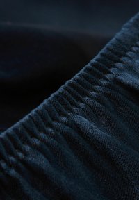 Mörk denimtyg med samlad elastisk detalj. Har en slät textur och en enhetlig blå färg som framhäver sömmar och tygväv.